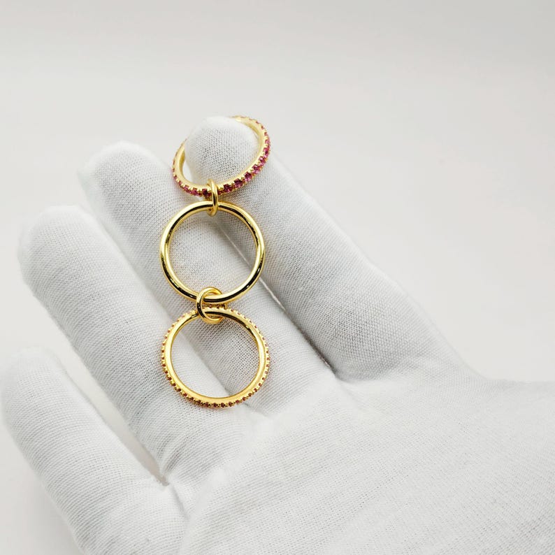 Peut inclure: Un ensemble de bagues dor&eacute;es avec trois anneaux reli&eacute;s. L'anneau sup&eacute;rieur est incrust&eacute; de petites pierres pr&eacute;cieuses rouges. Les deux autres anneaux sont en or uni. Les anneaux sont reli&eacute;s par de petites boucles dor&eacute;es.