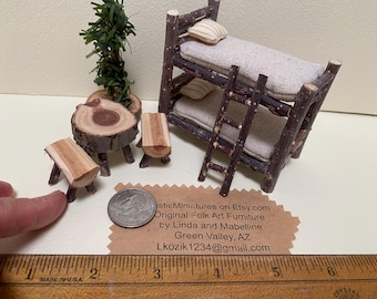 May include: A miniature bunk bed set made of dark brown twigs with light beige fabric mattresses and pillows, accompanied by a small round log table, two log stools, and a miniature tree. A US quarter coin and a wooden ruler are visible.