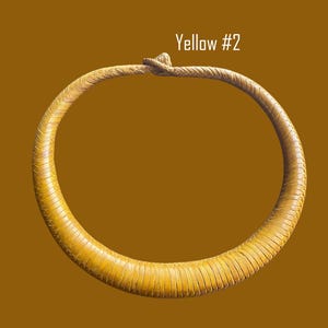 May include: A yellow necklace with a textured, stitched design. The necklace is a circular shape with a knotted closure. The text "Yellow #2" is displayed in white.