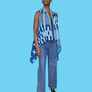 May include: A sleeveless vest with a blue and white geometric pattern. The vest is paired with blue jeans. The vest has a draped design and is made of a lightweight fabric. The jeans are a classic denim style.