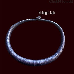 May include: A dark blue, textured necklace with the text "Midnight Kola" against a dark red background. The necklace is circular and appears to be made of a series of small, connected segments.