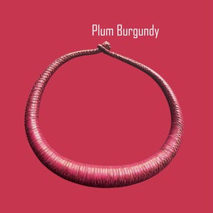 May include: A plum burgundy necklace with a textured, circular design. The necklace is set against a matching background, with the text "Plum Burgundy" in white.