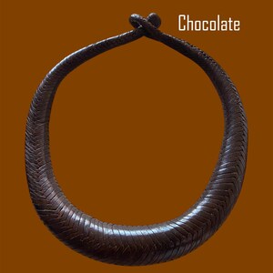 May include: A chocolate-colored, textured necklace with a circular design. The necklace is made of a woven material and features a knot closure. The word "Chocolate" is displayed in white text.