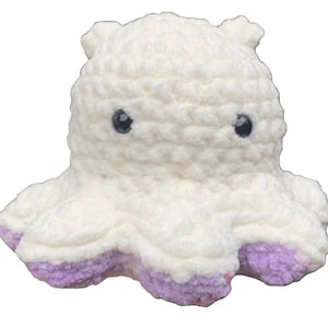 Puede incluir: Un juguete de peluche de pulpo blanco tejido a crochet con tentáculos de punta morada. El pulpo tiene ojos negros y una textura suave y peluda.