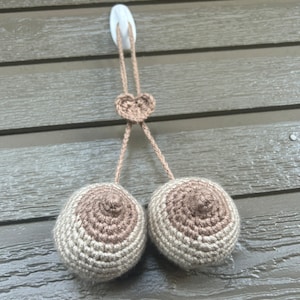 May include: Two crocheted brown and beige spheres hanging from a white hook with a crocheted heart at the top.