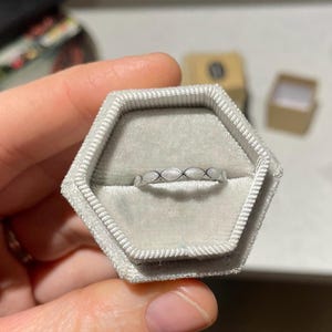 May include: A silver ring with a white enamel design in a gray ring box.