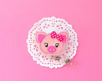 May include: Pink glitter pig with a pink bow and white polka dots, attached to a clear retractable badge holder.