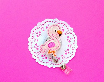 May include: Pink glitter flamingo charm with a white lace doily and a retractable badge holder.
