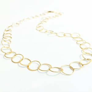 May include: A gold chain necklace with a delicate, open circle design. The chain is made of small, interconnected circles that create a flowing, elegant look.