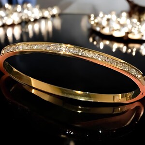 May include: A gold bangle bracelet with a row of clear cubic zirconia stones set in the band.