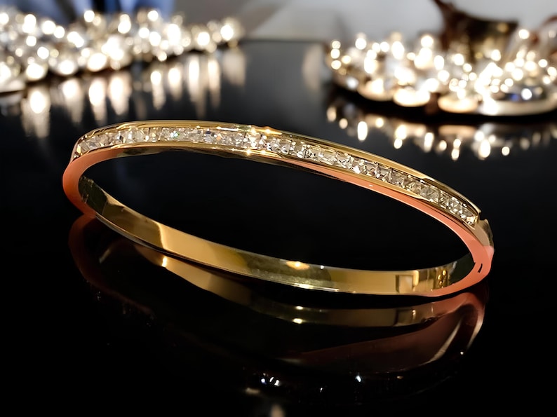 May include: A gold bangle bracelet with a row of clear cubic zirconia stones set in the band.