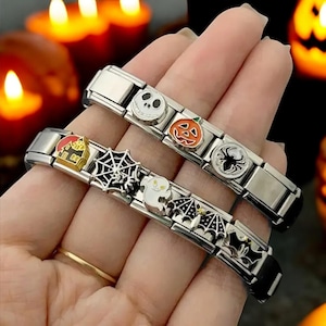 Puede incluir: Dos pulseras de plata con dijes de temática de Halloween. Los dijes incluyen un fantasma, una telaraña, una casa, una calabaza, un murciélago y una calavera. Las pulseras están en una mano sobre un fondo de calabazas iluminadas.