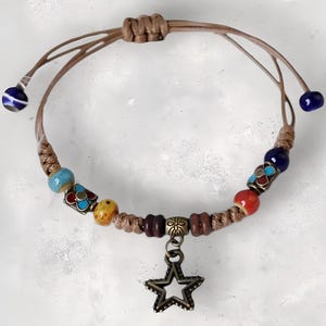 May include: A handmade bracelet featuring a woven cord with colorful beads in red, blue, yellow, and turquoise. The bracelet has a star-shaped charm and adjustable cord ends with blue and white beads. The bracelet is a bohemian style.