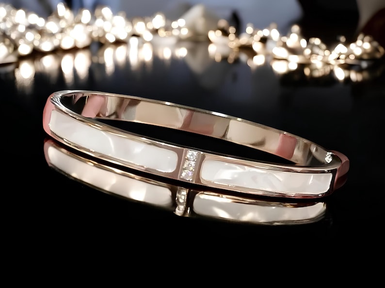 May include: A gold bangle bracelet with a white mother-of-pearl inlay and clear crystal accents.