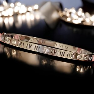 May include: A silver bangle bracelet with Roman numeral markings and small clear gemstones.