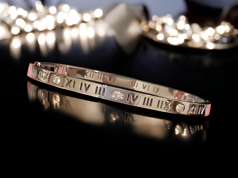 May include: A silver bangle bracelet with Roman numeral markings and small clear gemstones.
