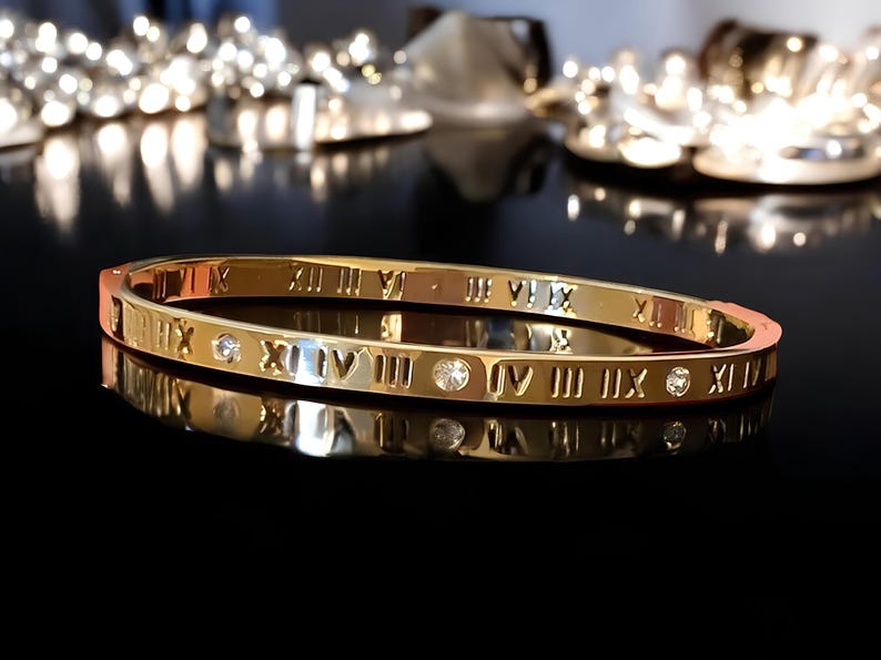 May include: A gold bangle bracelet with Roman numeral markings and small clear stones.