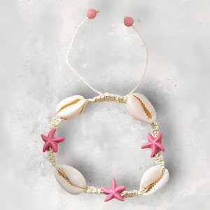 Op de afbeelding: Een wit en roze schelp- en zeesterarmband met een geknoopt koord.