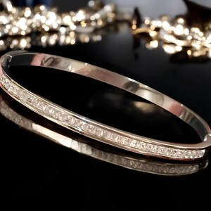 May include: A silver bangle bracelet with a row of clear cubic zirconia stones around the edge.