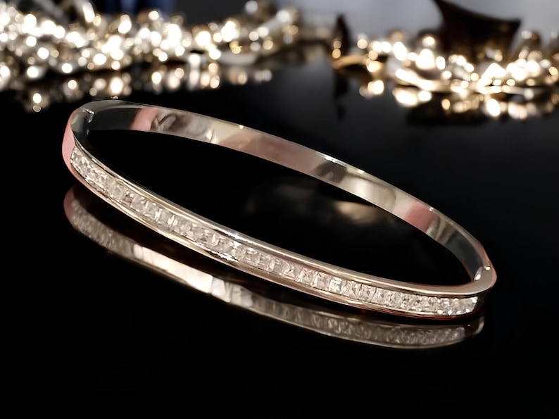 May include: A silver bangle bracelet with a row of clear cubic zirconia stones around the edge.