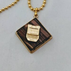 May include: A gold chain necklace with a square pendant featuring a brown and gold laptop design.