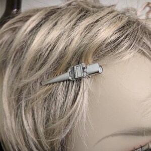 May include: A silver hair clip shaped like a wrench. The clip is about 2 inches long and has a textured surface.