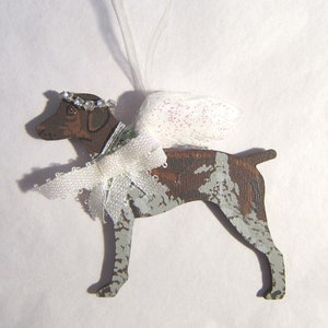 May include: Wooden dog ornament with angel wings and a halo. The dog is painted brown and white with a white ribbon bow and a string for hanging. A decorative item for pet lovers.