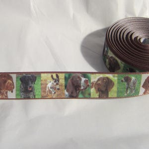 May include: Brown ribbon featuring a repeating pattern of various dog breeds. The ribbon is rolled up, with a section unrolled to display the dog portraits. The background is white.