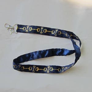 May include: A dark blue lanyard with gold equestrian-themed accents. The lanyard has a silver swivel clasp.
