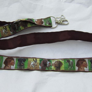May include: A brown lanyard with a silver key ring. The lanyard has a repeating pattern of different dog breeds, including a brown and white dog, a black and white dog, and a brown dog.