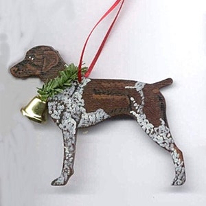 May include: A wooden Christmas ornament shaped like a German Shorthaired Pointer dog. The dog is painted brown and white with a green holly sprig around its neck and a gold bell hanging from the sprig.