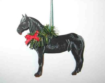 May include: A black horse ornament with a green wreath and a red bow around its neck. The horse is hanging from a green string. The ornament is made of wood and has a rustic appearance.