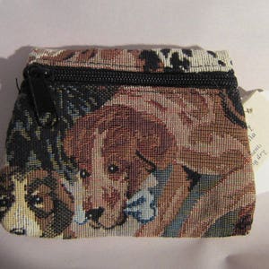May include: A small, brown, black, and beige zippered pouch with a tapestry design featuring dogs. The pouch has a black zipper and a black pull tab. The tapestry design features a variety of dog breeds, including a brown and white dog, a black and white dog, and a brown dog.