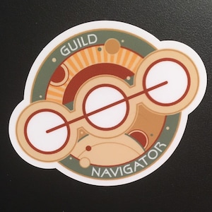 May include: A round sticker with a green, brown, and orange design. The sticker features three white circles with a line through them. The text "GUILD NAVIGATOR" is written around the edge of the sticker.