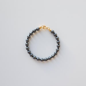 Puede incluir: Un brazalete de cuentas de hematites negras con un cierre dorado.