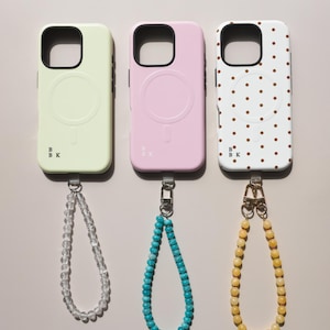 K&ouml;nnte beinhalten: Drei Handyh&uuml;llen in Pastellfarben: Hellgr&uuml;n, Rosa und Wei&szlig;. Jede H&uuml;lle hat einen schwarzen Rand und eine passende Armband-Kette. Die wei&szlig;e H&uuml;lle hat ein braunes Polka-Dot-Muster. Die H&uuml;llen haben ein kreisf&ouml;rmiges Design auf der R&uuml;ckseite.