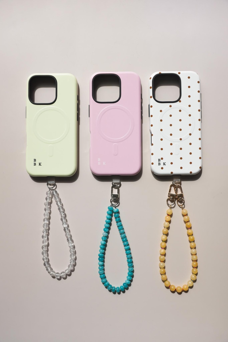 K&ouml;nnte beinhalten: Drei Handyh&uuml;llen in Pastellfarben: Hellgr&uuml;n, Rosa und Wei&szlig;. Jede H&uuml;lle hat einen schwarzen Rand und eine passende Armband-Kette. Die wei&szlig;e H&uuml;lle hat ein braunes Polka-Dot-Muster. Die H&uuml;llen haben ein kreisf&ouml;rmiges Design auf der R&uuml;ckseite.