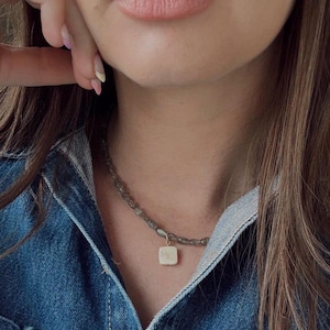 May include: A gold necklace with a square-shaped pendant made of a light-colored stone. The necklace is made of small, round, green beads.