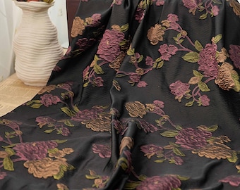 May include: Black fabric with a floral pattern in shades of purple, green, and gold. The fabric has a textured appearance, with the flowers appearing raised. The design features detailed floral and leaf motifs, creating a luxurious look.