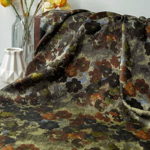 May include: A patterned fabric featuring a floral design in brown, orange, green, and blue hues. The fabric has a repeating pattern of stylized flowers on a muted background. The material appears soft and flowing, with a visible texture.