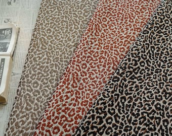 Puede incluir: Primer plano de tres muestras de tela con estampado de leopardo. Los colores incluyen marrón, rojo y negro. La tela es texturizada y parece ser un material tejido. Las muestras están dispuestas una al lado de la otra.