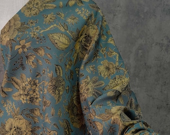 May include: Teal fabric with a detailed floral pattern in gold and brown tones. The design features various flowers, leaves, and botanical elements. The fabric is draped over a mannequin, showcasing the intricate print and texture.