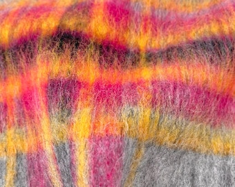 May include: Close-up of a soft, textured textile with a plaid pattern. The design features vibrant colors, including shades of pink, orange, and yellow, set against a gray background. The fabric appears to be fluffy and warm, suggesting a cozy blanket or scarf.
