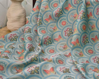 Könnte beinhalten: Ein drapiertes Gewebe mit einem sich wiederholenden Muster aus hellblauen Kreisen, die jeweils ein stilisiertes Vogel-, Schmetterlings- und Blumendesign in Rot, Orange und Grün enthalten. Der Stoff hat einen subtilen Glanz und ein weiches, fließendes Aussehen.