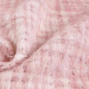 May include: Close-up of a soft, textured fabric in shades of pink and white. The material has a fuzzy, almost fur-like appearance, with a subtle pattern. The fabric appears to be a luxurious textile, possibly for clothing or home decor.