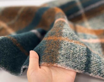 May include: Close-up of a folded fabric with a plaid pattern. The fabric features a teal, brown, and orange color scheme. The texture appears soft and fuzzy, with a visible weave. The plaid design is composed of intersecting stripes.
