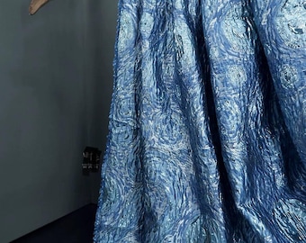 May include: A draped fabric in shades of blue, with a shimmering, iridescent quality. The fabric is patterned with swirling, circular designs, creating a visual texture. The fabric is hanging from a wooden branch.