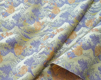 May include: Cream fabric featuring a repeating design of stylised ocean waves in blue and purple hues. Orange floral details are interspersed throughout. The fabric is draped, showing a glimpse of a brown patterned underside.