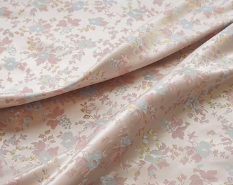 May include: A close-up of a pale pink floral fabric with a satin sheen. The fabric features a repeating pattern of pink and light blue flowers with gold accents. The fabric is draped, showing folds and texture.