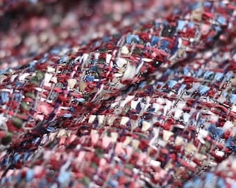May include: Close-up of a textured fabric with a woven pattern. The fabric features a mix of colours, including red, white, blue, and silver threads. The weave creates a complex, multi-dimensional appearance, suitable for apparel or home decor.